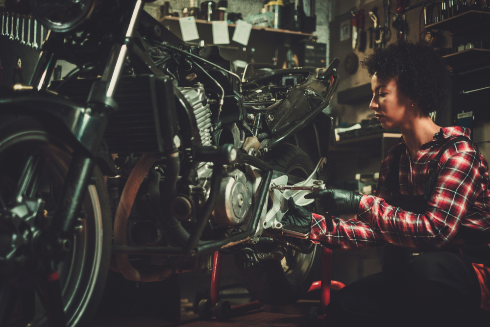 A women next to her motorcycle working on the engine in a workshop.
