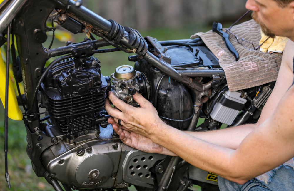 A close up of someone working on their motorcycle with grease on their hands.