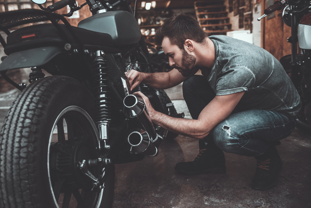 A man crouching next to his motorcycle working on it in a workshop.